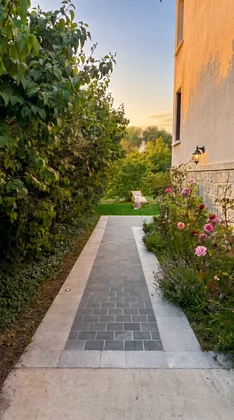 Allée pavée bordée de rosiers en fleurs menant au jardin au coucher du soleil