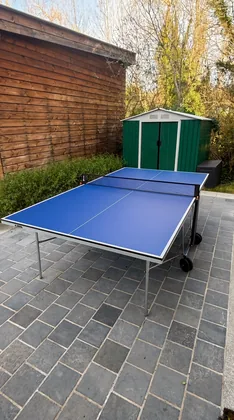 Table de ping-pong bleue installée sur la terrasse carrelée du jardin
