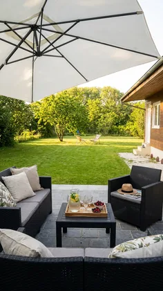 Terrasse avec salon de jardin, parasol et plateau apéritif, vue sur la pelouse et la dépendance