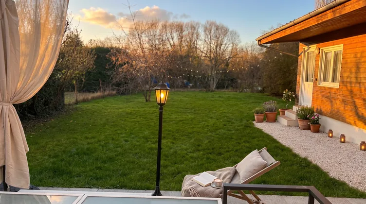 Jardin au coucher du soleil avec transat, rideau voilage, lampadaire et bougies sur le rebord de la dépendance