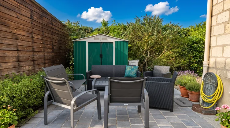 Salon de jardin avec chaises et canapé sur la terrasse carrelée par beau temps