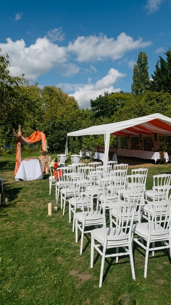 Chaises blanches installées sur la pelouse face à une arche décorée pour une cérémonie